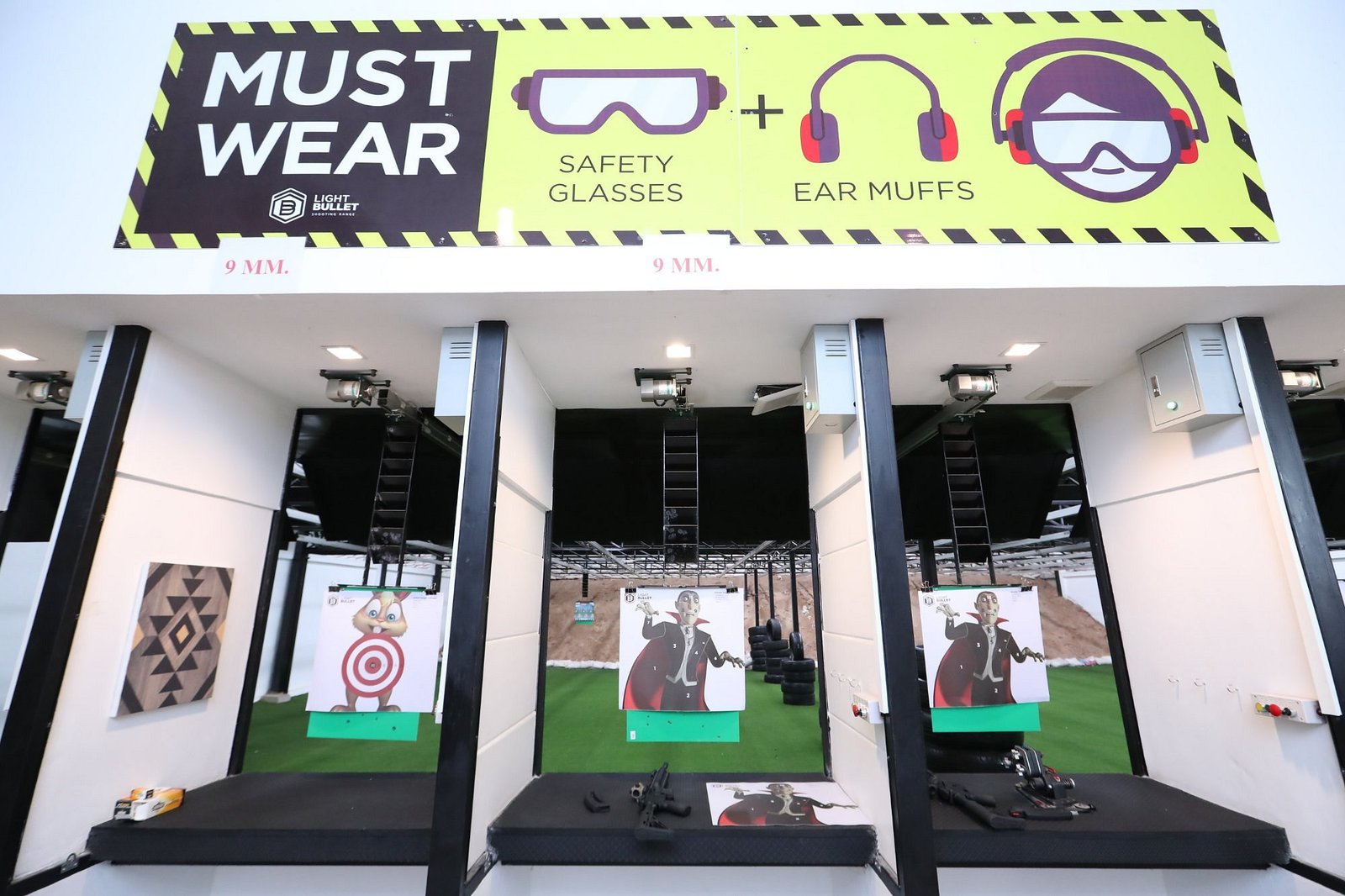 Bright indoor pistol booths with safety signage and targets at Light Bullet